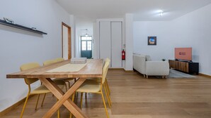 A modern living room with a wooden dining table, yellow chairs, a sofa, and a TV. - GuestReady - Doctor House Gardens (Horta)