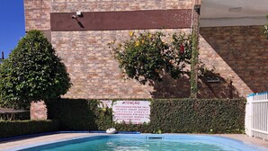Una piscina nítida amb un objecte blau flotant al centre, envoltada per una paret de maó i vegetació.