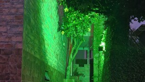 Un camí estret vora parets de maó i vegetació, que condueix a l'entrada d'un edifici.