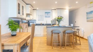 A modern kitchen with white cabinets, a wooden dining table, and bar stools. - 2 Bed in Port Isaac (oc-l50168) (Port Isaac)
