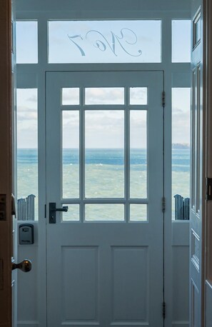 Eine weiße Tür, durch ein Fenster ist Meerblick.