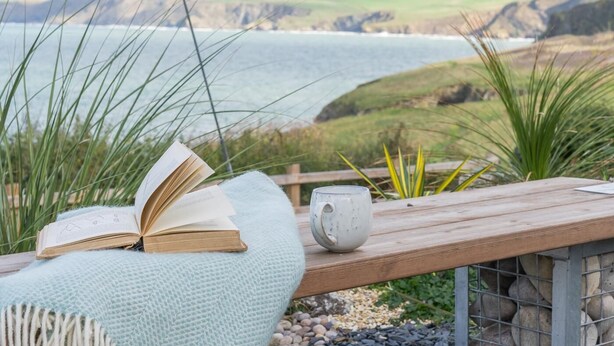 An open book on a wooden bench with a view of the sea and cliffs. - 2 Bed in Port Isaac (oc-l50105) (Port Isaac)