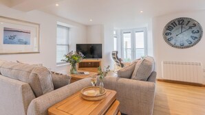 A modern living room with a large clock, a flat-screen TV, and a sofa set. - 2 Bed in Port Isaac (oc-l50105) (Port Isaac)