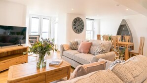 A living room with a TV, sofa, coffee table, and a clock on the wall. - 2 Bed in Port Isaac (oc-l50105) (Port Isaac)