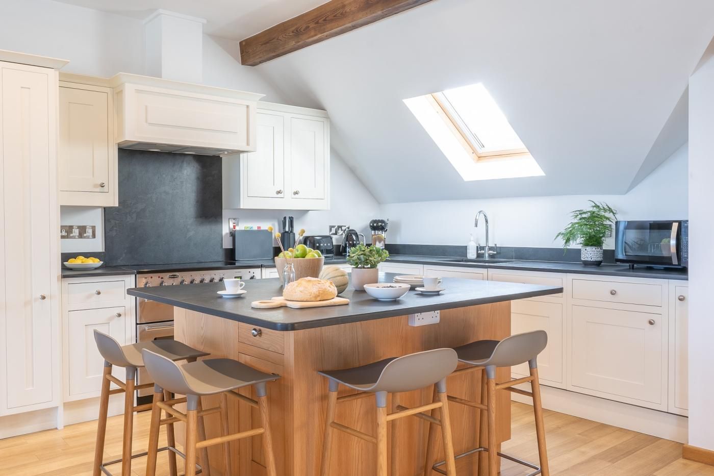 A modern kitchen with a central island, bar stools, a skylight, and a microwave.
