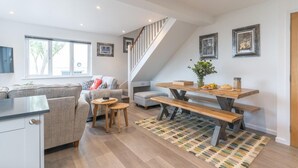 En moderne opholdsstue med trappe, spiseområde med et træbord og bænke, sofa og et køkken.