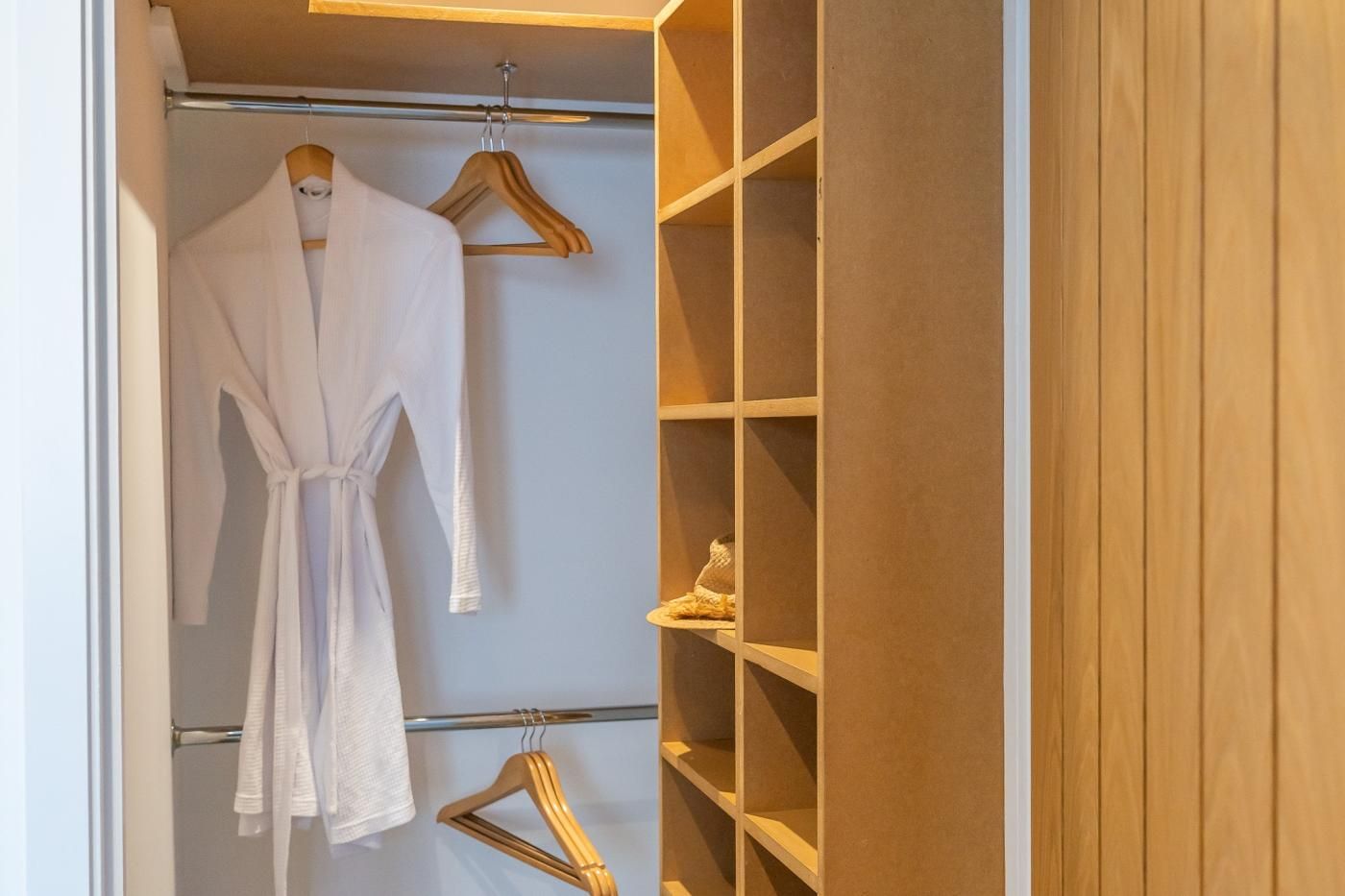 Un dressing où l’on peut entrer, avec une robe suspendue à un cintre en bois, une tringle en métal et des étagères remplies de chaussures.