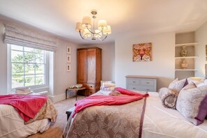 A bedroom with two beds, a wooden wardrobe, a chandelier, a window with a view, and a shelf with decorative items. - 7 Bed in Awre (oc-b42471) (Awre)