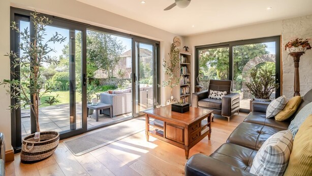 A spacious living room with a sofa, a coffee table, and a bookshelf. Large sliding glass doors open to a garden. - 7 Bed in Awre (oc-b42471) (Awre)
