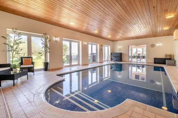 An indoor swimming pool with a wooden ceiling, large windows, and a seating area with chairs and a table. - 7 Bed in Awre (oc-b42471) (Awre)