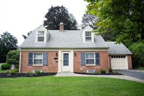 A two-story brick house with a front garage, a front door, and two windows with shutters.