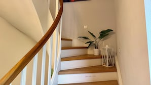 Eine Treppe mit Holzdielen und einem Holzgeländer, eine Topfpflanze und ein weißer Laternenleuchter auf der Landung.