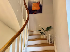 Eine Treppe mit Holzdielen und einem Holzgeländer, eine Topfpflanze und ein weißer Laternenleuchter auf der Landung.