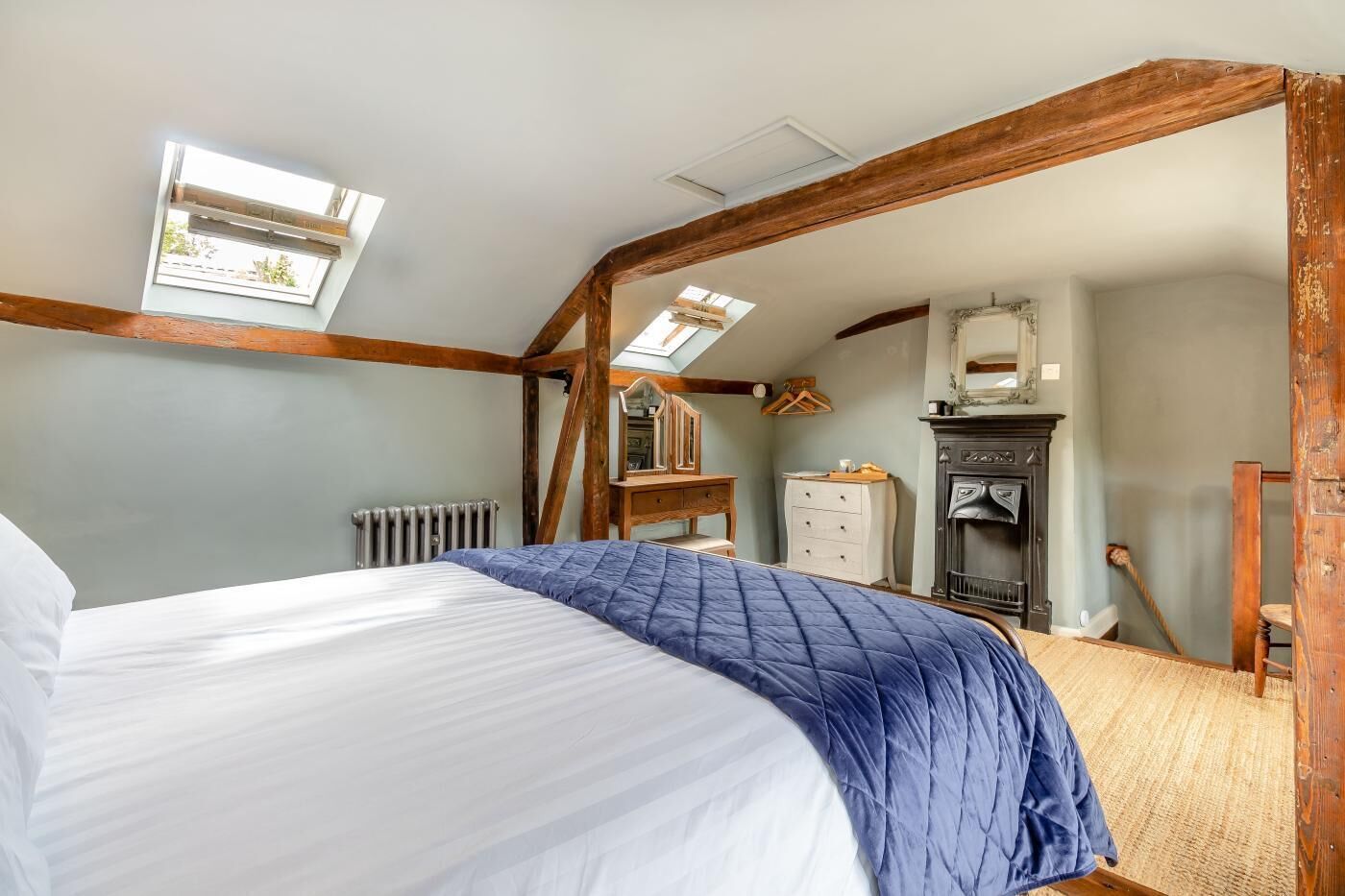 A bedroom with a bed, a dresser, a mirror, a radiator, and a fireplace.