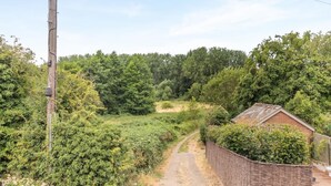 Ett lantligt landskap med en grusväg som leder fram till en byggnad av tegel, omgiven av tät vegetation.