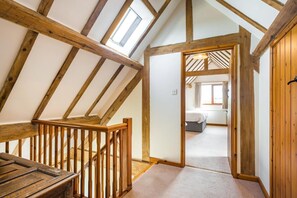 Ein Zimmer mit schrägen Wänden, Holzbalken, einer Treppe und einem Bett.