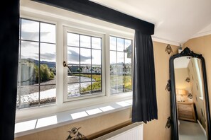 A room with a large window, a radiator below, and a mirror with decorative elements. - 4 Bed in Keswick (oc-s42744) (Keswick)
