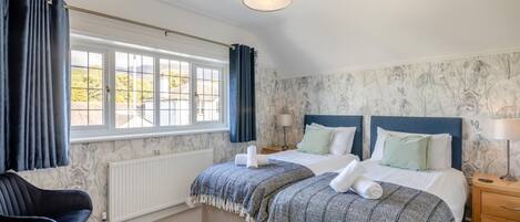 Een slaapkamer met twee bedden, een raam met gordijnen, een radiator, een stoel en een nachtkastje met een lamp.