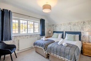 Ein Schlafzimmer mit zwei Betten, einem Fenster mit Vorhängen, einem Heizkörper, einem Stuhl und einem Nachttisch mit Lampe.