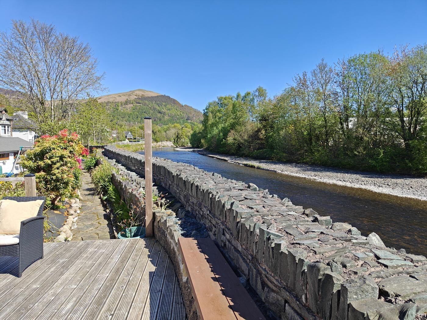 A stone bridge over a river, a wooden deck, and a hillside in the background.