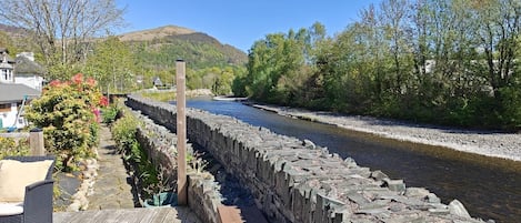 A stone bridge over a river, a wooden deck, and a hillside in the background.