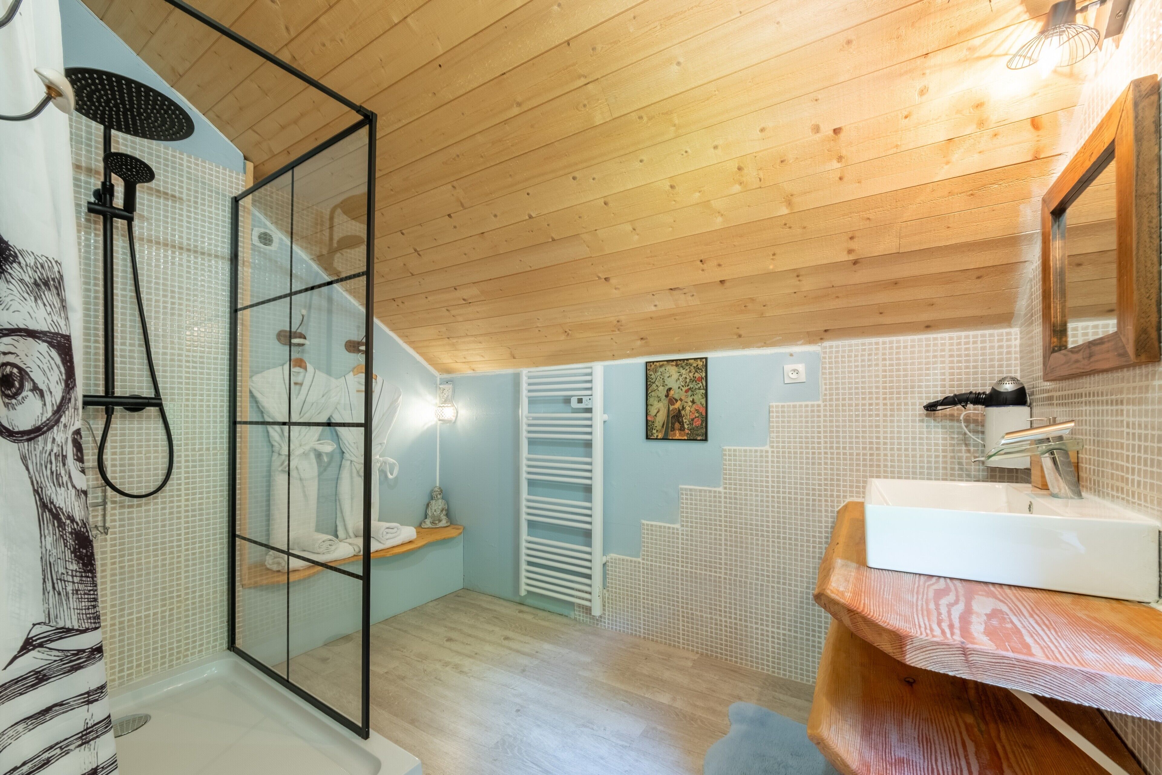 A modern bathroom with a glass shower enclosure, a wooden ceiling, a white sink, and a tiled floor.