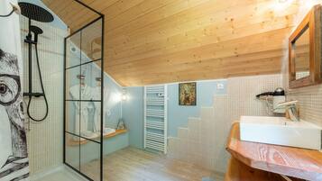 A modern bathroom with a glass shower enclosure, a wooden ceiling, a white sink, and a tiled floor.