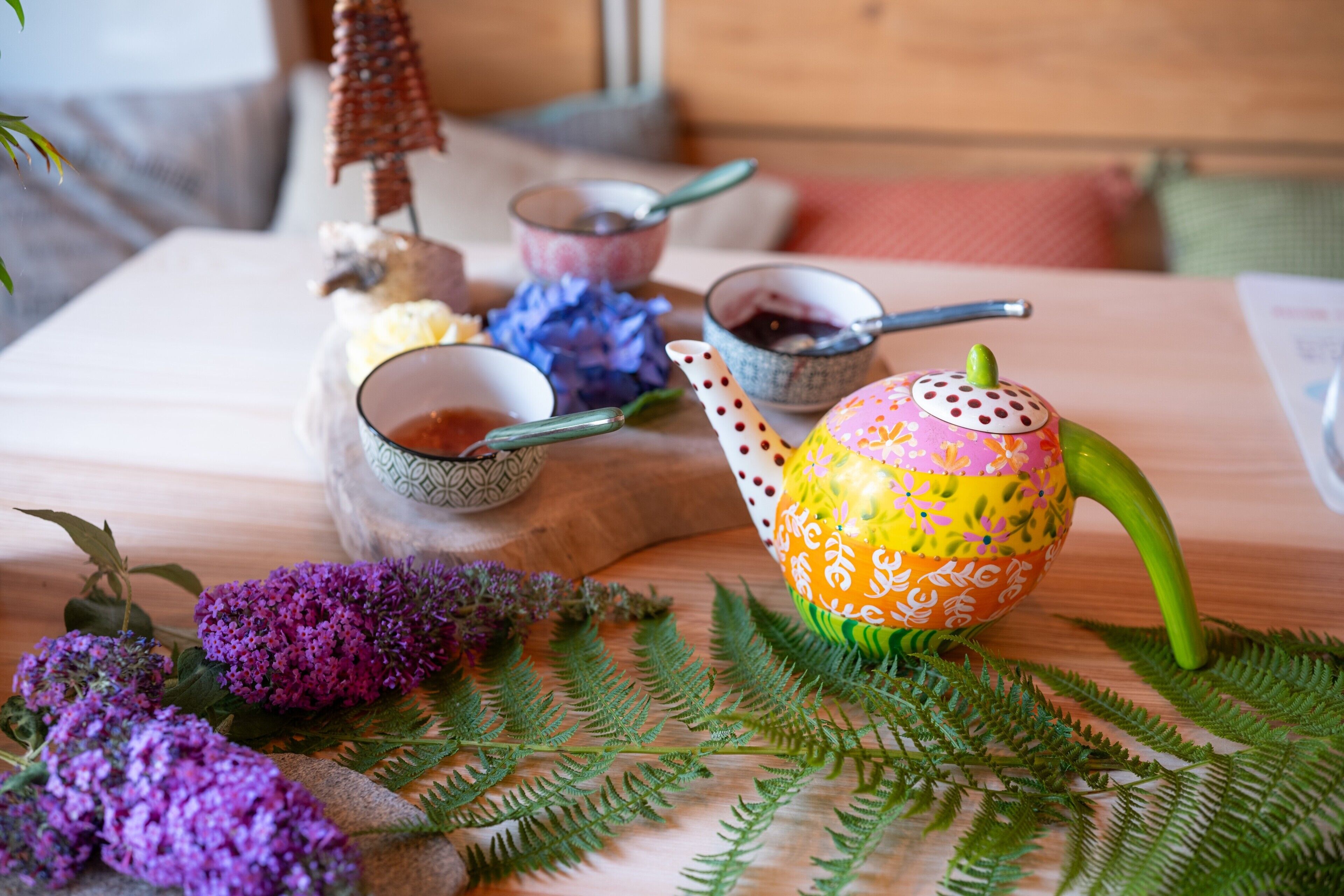 Een houten tafel met een decoratieve theepot, een kleine kom en een lepel.