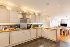 A modern kitchen with a central island, stainless steel appliances, and a dining area with a TV. - 3 Bed in Croyde (oc-s44806) (Croyde)