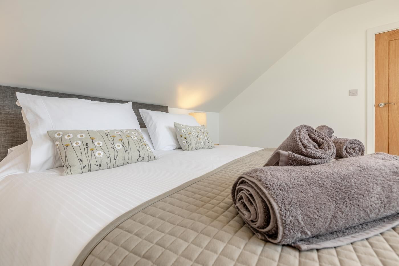A bedroom with a bed, pillows, a rolled-up towel, and a door.