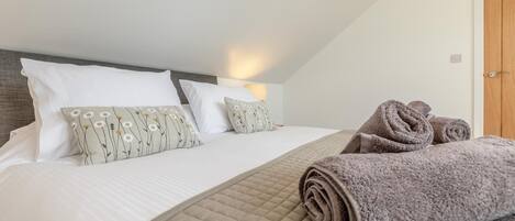 A bedroom with a bed, pillows, a rolled-up towel, and a door.