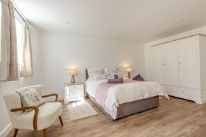 Ein Schlafzimmer mit Bett, Nachttischen, einem Sessel, einem Kleiderschrank und einem Fenster mit Vorhängen.