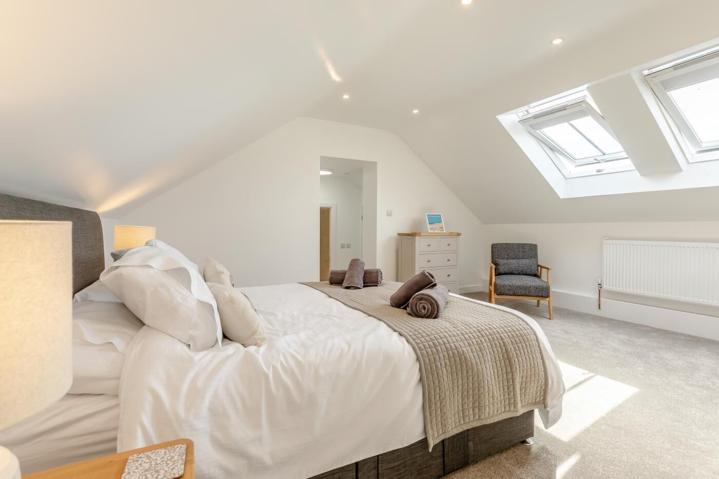 A bedroom with a bed, a chair, a dresser, a radiator, and skylights.