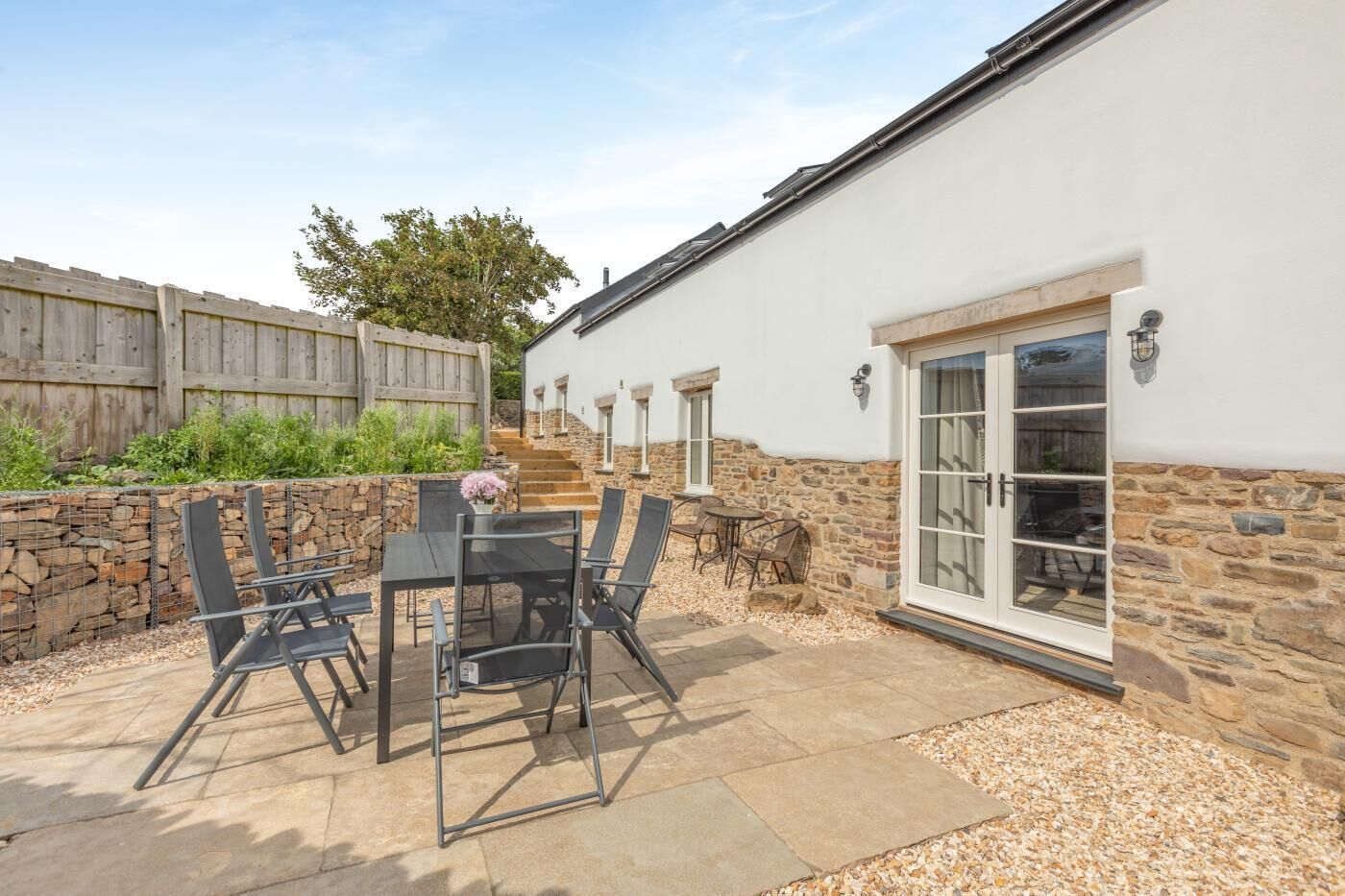 A patio with a table and chairs, a stone wall, and a white building with a stone foundation.