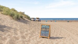 Ein Strand mit einem Schild, das Grillen und offenes Feuer am Sand verbietet, und einer Warnung, dass Hunde nicht erlaubt sind.