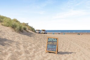 Ein Strand mit einem Schild, das Grillen und offenes Feuer am Sand verbietet, und einer Warnung, dass Hunde nicht erlaubt sind.