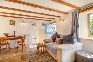 A cozy living room with a wooden ceiling, a sofa with cushions, a small table with a lamp, and a window with curtains. - 1 Bed in Ruan Minor (oc-rencot) (Ruan Minor)