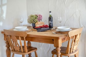 A wooden dining table with two chairs, a bottle of El Monjarrib wine, a loaf of bread, a bowl of red berries, and a vase of flowers. - 1 Bed in Ruan Minor (oc-rencot) (Ruan Minor)