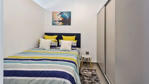 Ein Schlafzimmer mit Bett, Kissen, einem Gemälde, einem kleinen Tisch und einem Kleiderschrank.