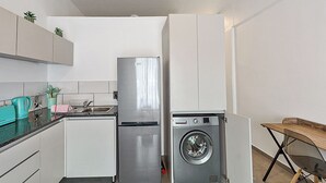 Eine kompakte Küche mit Kühlschrank, Waschmaschine und einem kleinen Esstisch.