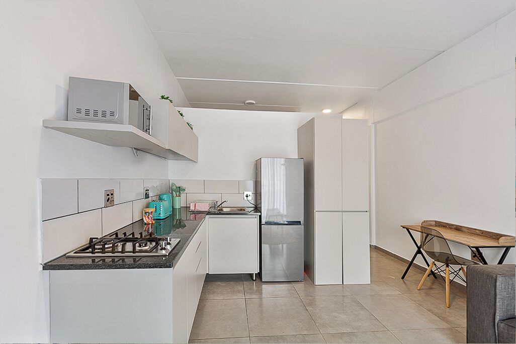 A modern kitchen with white cabinetry, a gas stove, a stainless steel refrigerator, and a wooden dining table.