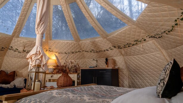A cozy tent with a quilted exterior, a bed with patterned bedding, a bedside lamp, and a small table with decorative items. - 1 Bed in Hanworth (oc-p43298) (Hanworth)