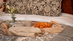 A bed with a patterned pillow, a tray with croissants, a vase with flowers, and two cups. - 1 Bed in Hanworth (oc-p43298) (Hanworth)