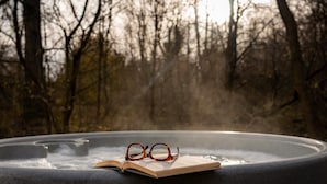 A hot tub with a book and glasses on it, surrounded by trees.
