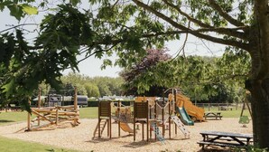 Een speeltuin met diverse speeltoestellen, picknicktafels en een gazon.