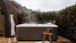 Een hottub op een houten terras, met een witte handdoek en badjas in de buurt, omringd door groen en sfeerverlichting.