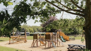 Un parque infantil con diversas estructuras de juego, mesas de picnic y una zona de césped.