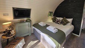 A bedroom with a bed, a television, a small table with a lamp, and a bench.