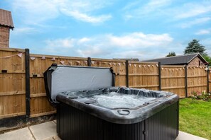 Un jacuzzi en un entorno al aire libre con un cerco de madera y una casa al fondo.