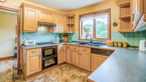 A kitchen with wooden cabinets, a built-in oven, a dishwasher, and a window with a view of greenery. - 3 Bed in Balmaclellan (oc-i44754) (Balmaclellan)